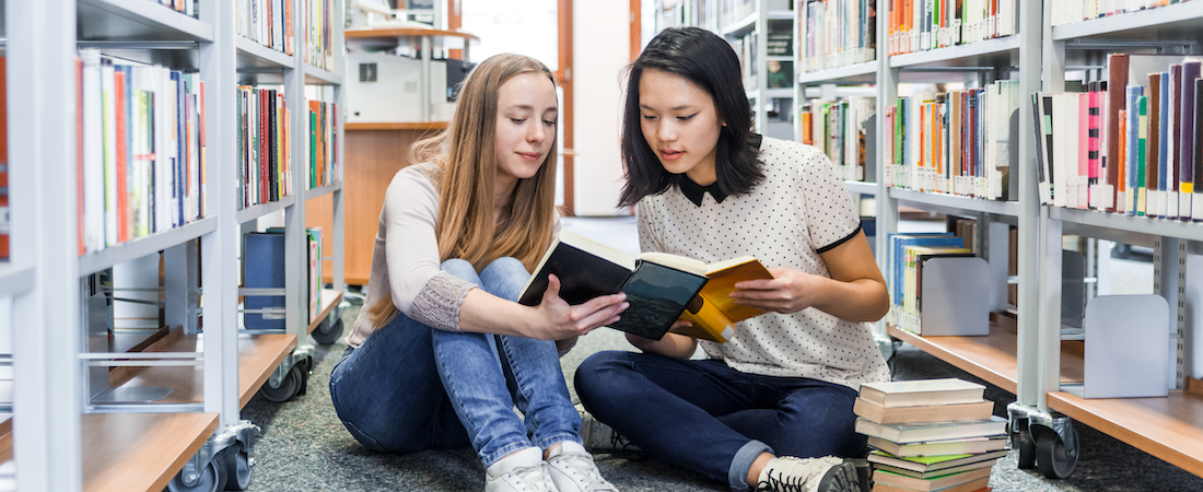 Two students sitting in a library reading books.