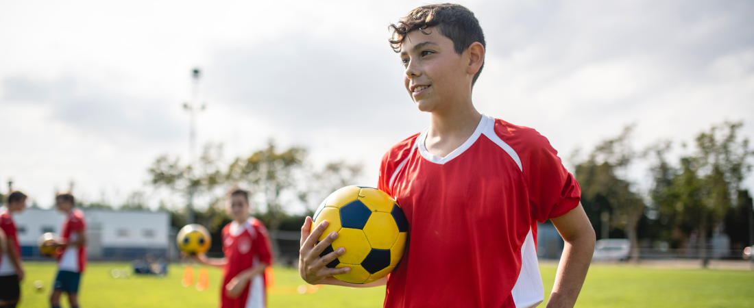 Un jugador de fútbol adolescente sostiene un balón mientras está en una cancha junto con su equipo. Este blog explica los riesgos del vapeo para los atletas adolescentes.