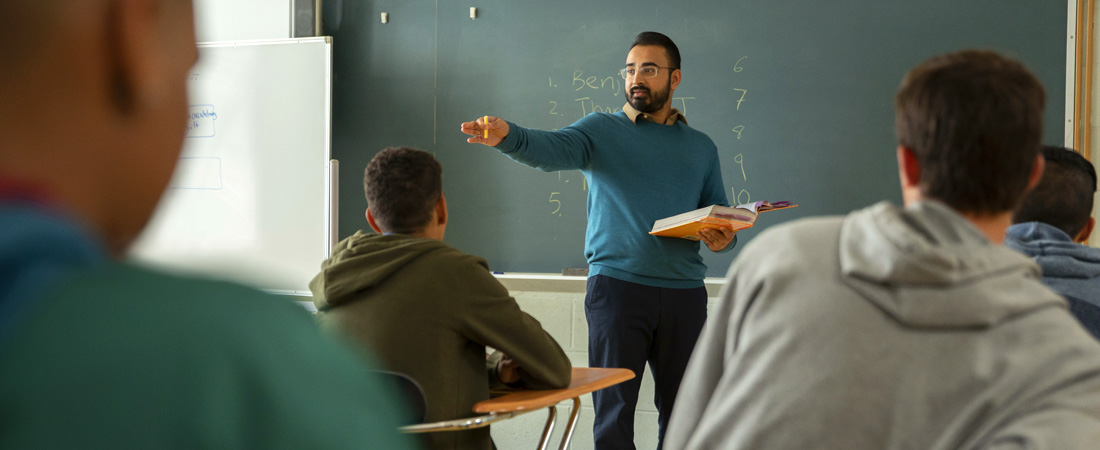 teacher with book at chalkboard, calling on a student for an answer
